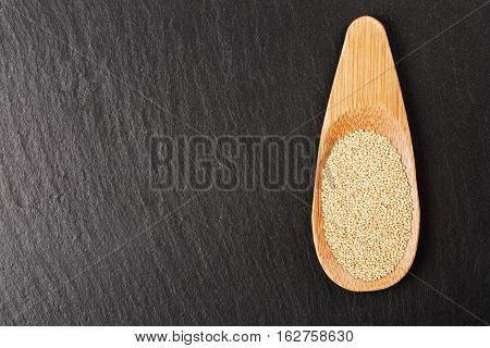 Raw white amaranth seeds in wooden spoon on black stone background. Concept of healthy and gluten free food.