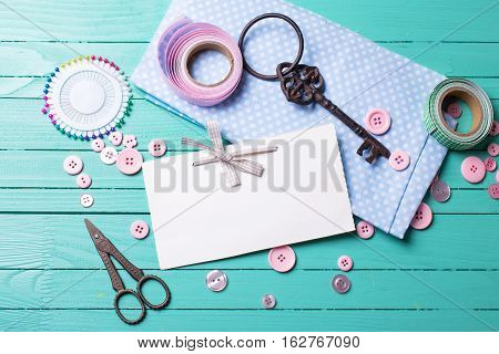 Sewing thread - buttons scissors fabric and empty tag on turquoise wooden background. Selective focus. Scrapbboking. Flat lay. Place for text.