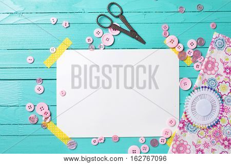 Sewing thread - buttons scissors fabric and empty tag on turquoise wooden background. Selective focus. Scrapbboking. Flat lay. Place for text.