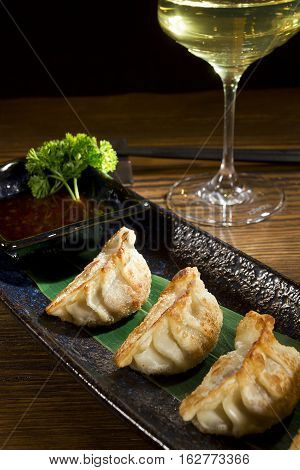 Yaki gedza with sauce in a ceramic pot on a wooden table
