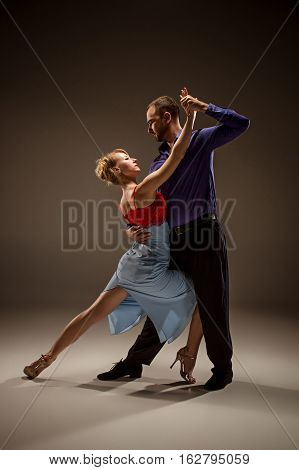 A man and a woman dancing argentinian tango on gray studio background