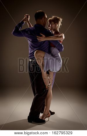 A man and a woman dancing argentinian tango on gray studio background