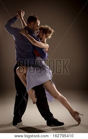 A man and a woman dancing argentinian tango on gray studio background