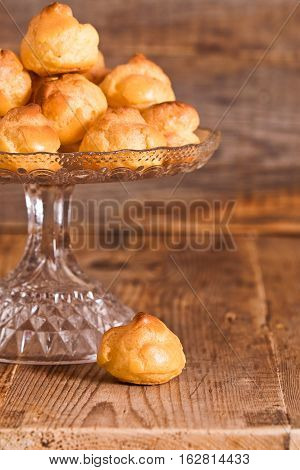 Sweet cream puffs on glass tray on wooden table.