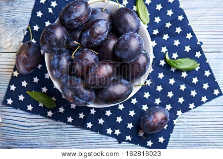 Fresh organic plums in ceramic bowl on rustic wooden table at dark napkin with stars.