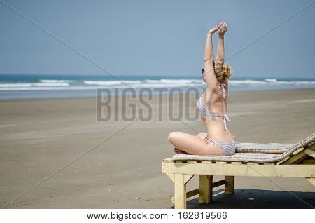 blonde girl in bikini doing yoga on a sun lounger on the ocean