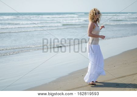curly blonde girl on the background of the sea in a white long skirt