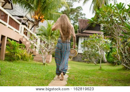 Blonde girl with long hair goes in a green tropical garden