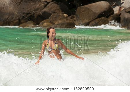 Happy young woman playing with crashing waves in sunny day