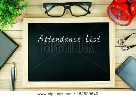 Top view of pen, diary, plant, eye glasses, alarm clock, smartphone, earphone and chalkboard written with ATTENDANCE LIST on wooden background. Business Concept.