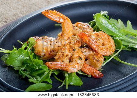 close up with fresh fried shirmps with arugula on a black plate