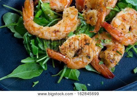 close up with fresh fried shirmps with arugula on a black plate