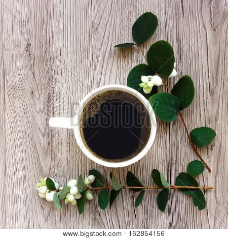 Cup of black coffee decorated with green branches of ghostberry on wooden table. Top view flat lay view from above