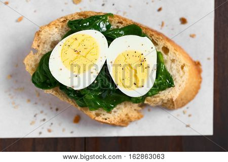 Crostini roasted bread slice with cooked spinach leaves and hard boiled quail eggs seasoned with black pepper photographed overhead with natural light (Selective Focus Focus on the top of the egg halves)