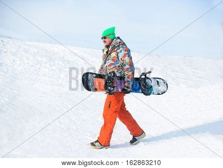 Snowboarder Walking Against Snowy Mountains And Blue Sky