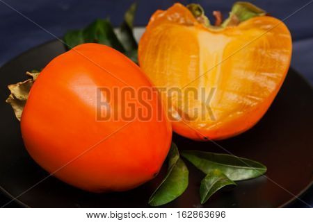 Fresh organic persimmon fruit cut in half close-up on dark background. Concept for healthy food, vegan or raw diet.