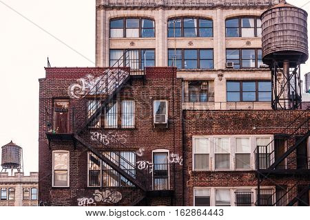 Back side of a brick apartment building in Manhattan, showing the fire escape and graffiti on its facade.