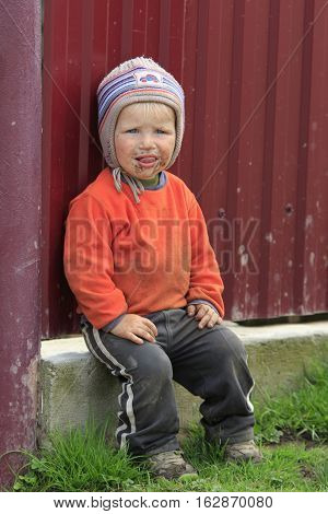 STINKA UKRAINE - APRIL 14 2016 - funny little dirty boy with his tongue out sits at the fence on April 14 2016 in Stinka village