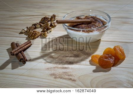Creamy rice pudding with cinnamon sticks, walnuts and dried apricots on a wooden table