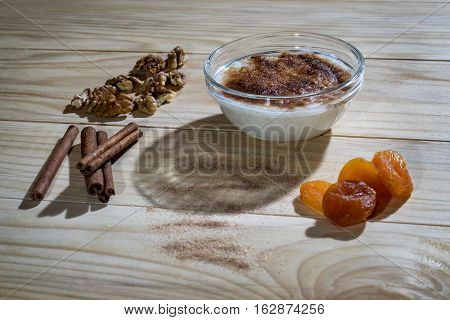 Creamy rice pudding with cinnamon sticks, walnuts and dried apricots on a wooden table