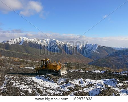 Crawler tractor with grederom against the backdrop of snow-capped mountains. Alignment grederom area for technological needs.