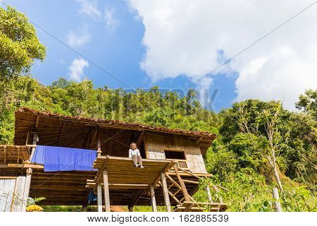 Happy woman dangle her legs with smiling face on a small thatched cottage in Ban Pa Pong Piang Chiang Mai province Thailand