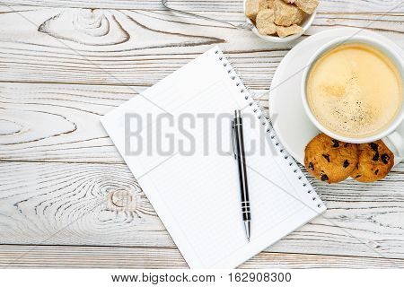 Still life with cup of coffee and note pad on light wooden table