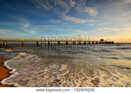 Beautiful scenery of sunset sky at beach with wave motion at foreground and long jetty at background. Motion blur on the foreground due to slow or fast shutter speed shot. Composition of nature.