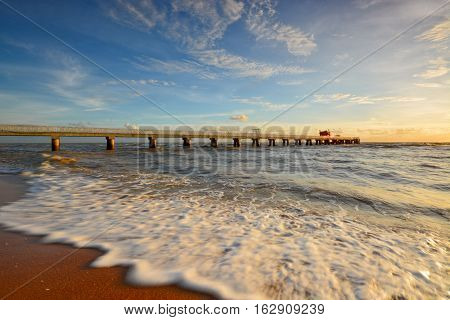 Beautiful scenery of sunset sky at beach with wave motion at foreground and long jetty at background. Motion blur on the foreground due to slow or fast shutter speed shot. Composition of nature.
