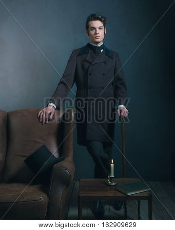 Retro Dickens Style Man Standing With Cane Next To Leather Chair.