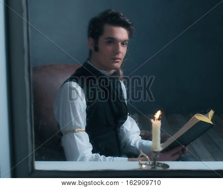 Vintage Victorian Man Sitting By Rainy Window Reading Book With Candlelight.