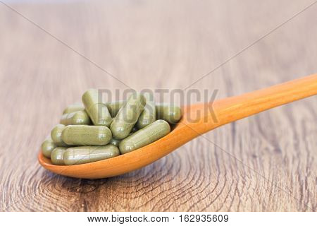 Green Herb Powder Capsules On Wooden Spoon