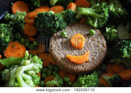 Vegan food: smiling soy burger and vegetables.