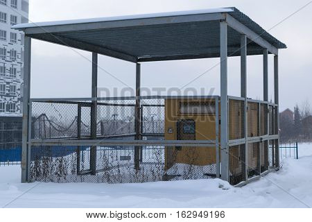 several diesel generators yellow stand under a canopy is fenced with a metal grid lying on the street white snow winter sky fog smog