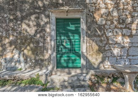 Typical house green door in Tucepi old village in the slope of a mountain Biokovo. Tree shadow texture on the facade.