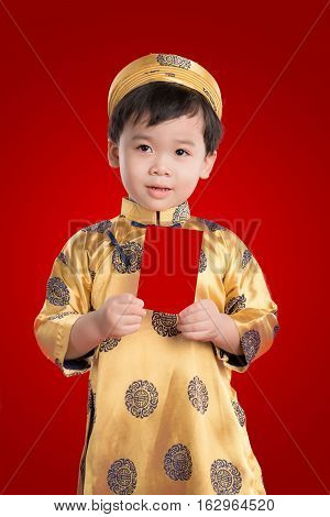 Cheerful boy wearing ao dai dress holding greeting cards for Tet holiday. It is the gift in lunar new year or Tet Holiday on red isolate background.