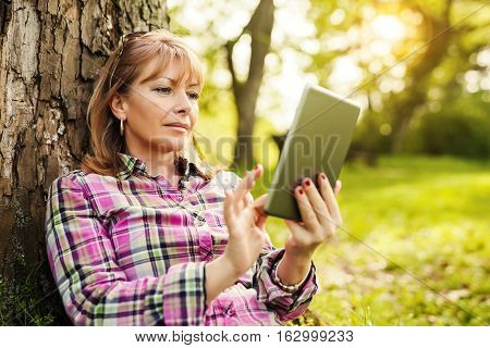 Beautiful mature woman in the park using a digital tablet.