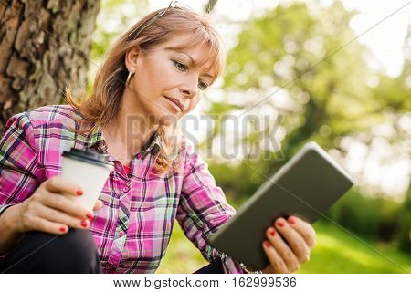 Beautiful mature woman in the park using a digital tablet.