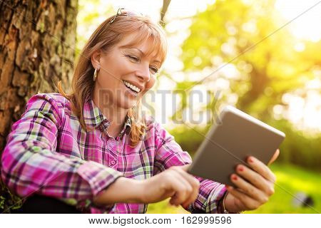 Beautiful mature woman in the park using a digital tablet.Relaxing in nature.