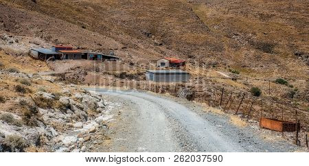 Road Winding Through Arid Mountains Past Farm