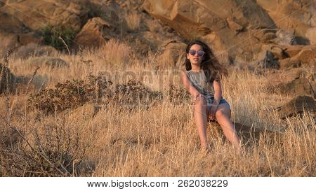 Teen Sitting In Dry Brush On The Side Of A Mountain With Sun Purple Glasses
