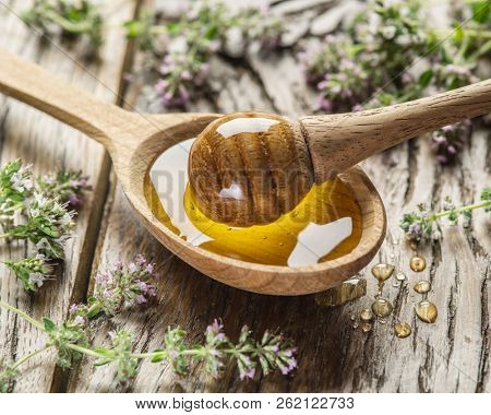 Herbal honey pouring into the wooden spoon. Spoon is on old wooden table surrounded with levender flowers.