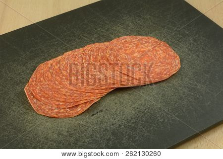Close Up Of Uncured Salami Meat Slices On Black Cutting Board
