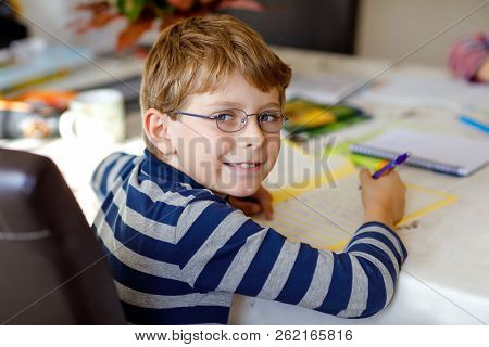 Happy Smiling Little Kid Boy With Glasses At Home Making Homework At The Morning Before The School S