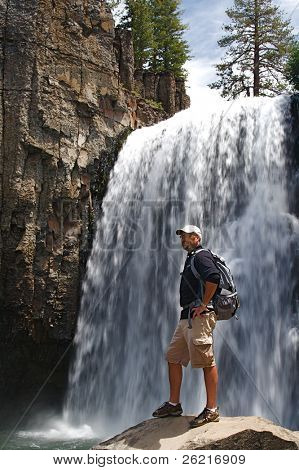 Hiker ทนทานมองภูมิประเทศป่าที่น้ำตกสายรุ้งใน NM Postpile ปีศาจ