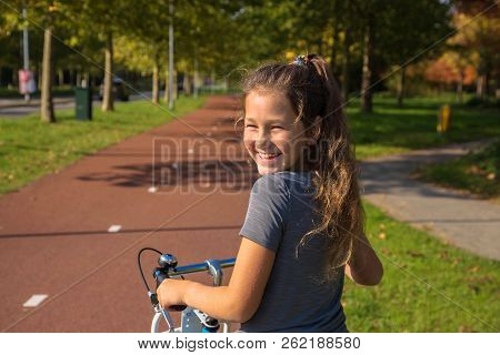 Happy Child Rides A Bike On Bike Path. Cyclist Child Or Teenager Girl Enjoys Good Weather And Cyclin