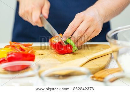 Men's Hands Cut Red And Yellow Pepper On The Wooden Board Close Up
