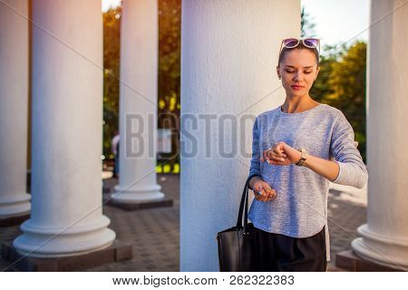 College Student Waiting For Friends In Park. Young Woman Checking Time Looking At Watch