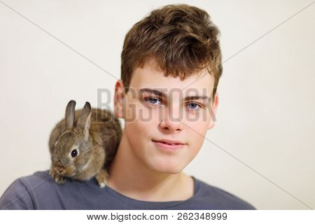 Handsome smiling boy teenager with rabbit on the shoulder poses in white studio