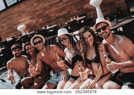 Young Friends With Alcoholic Drinks At Poolside. Group Of Young Smiling People Holding Bottles Of Be